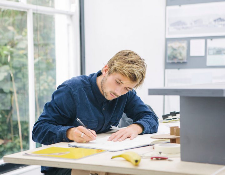Falmouth University Architecture student working at a desk, wearing a blue shirt