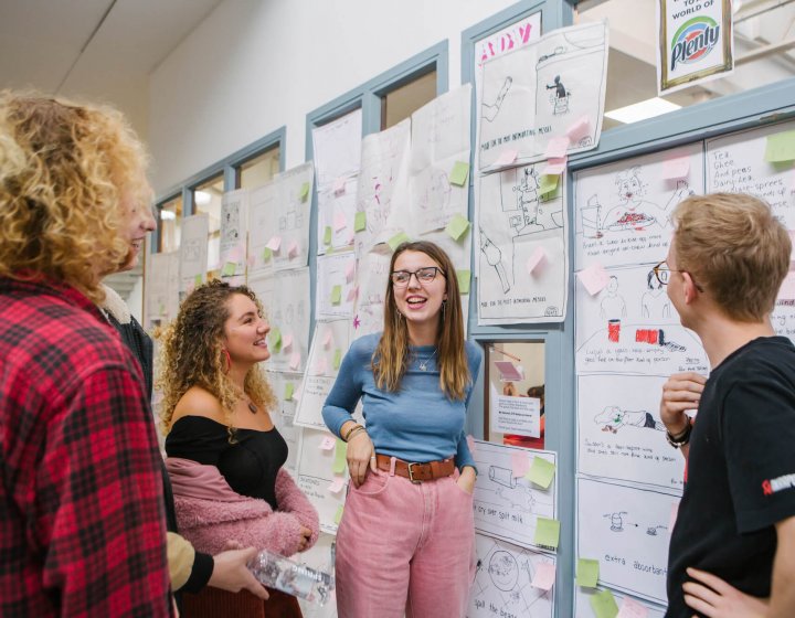 Creative advertising students discussing in front of an ideas wall.