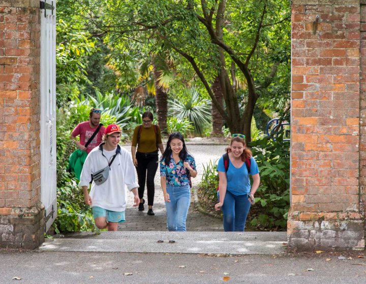Students walking towards a gateway between red brick walls on Falmouth campus.