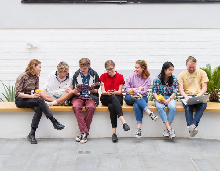 A group of Falmouth University students sitting on a wall inside a white building
