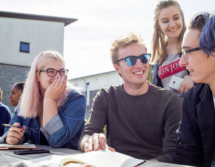 Students sat at bench outside with sunglasses and smiling.