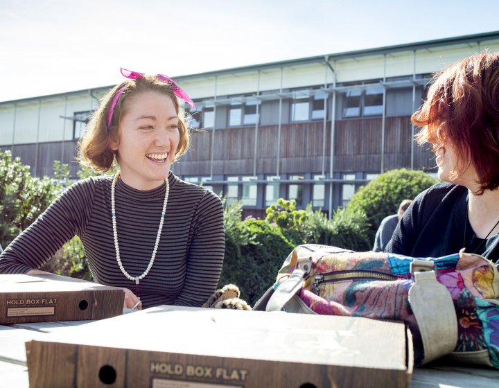 Student smiling with pink head scarf and pizza boxes on table.