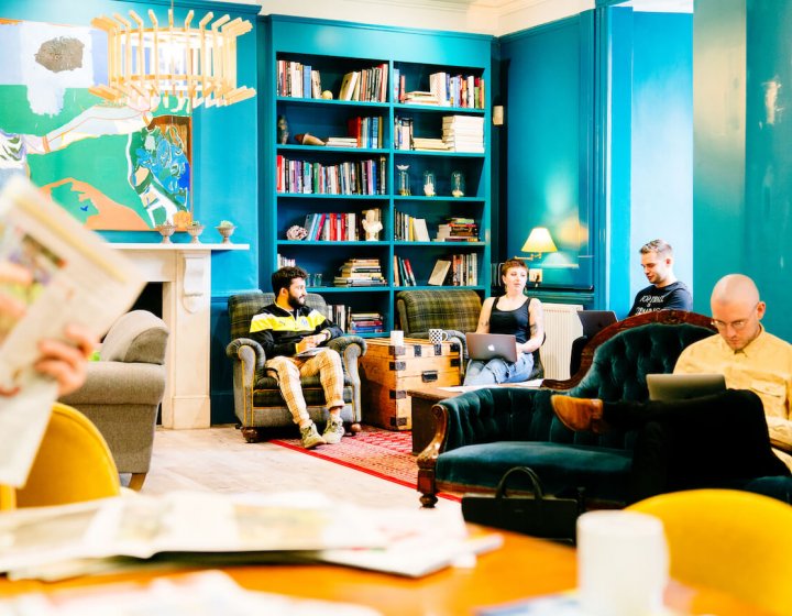 A group of students seated on sofas in a blue room with book cases and art on walls