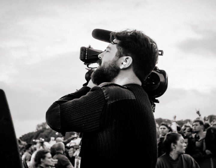 Place and white image of a man using a film camera with a crowd in the background