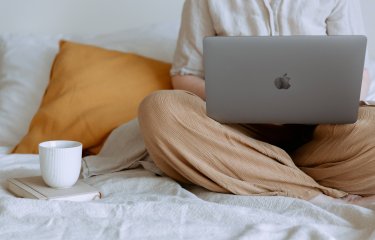 A person sat crossed legs with an apple mac and a cup
