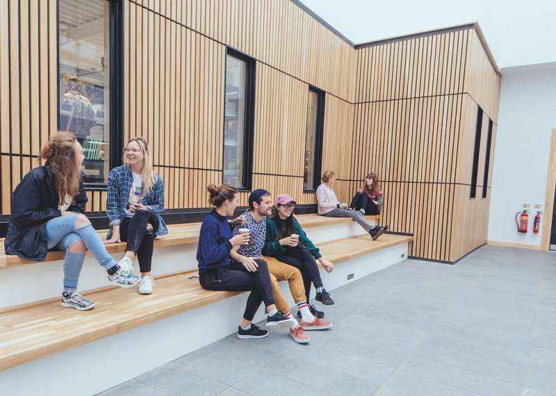 Falmouth University students sitting on steps with a wooden cladded wall behind