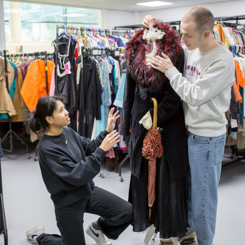 Two students working on a long coat on a mannequin in the Wardrobe Store